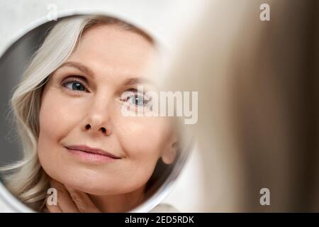 Happy 50s Frau mittleren Alters berühren Gesicht Haut Blick in Spiegelreflexion. Stockfoto