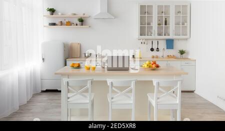 Bunte Früchte, Orangensaft in Glas und Krug, graue Tasse auf dem Tisch, Utensilien auf weißen Möbeln Stockfoto