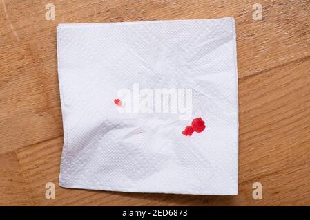 Tropfen von echtem Blut auf zerknitterter Papierserviette. Blutige Serviette auf Holzboden. Stockfoto