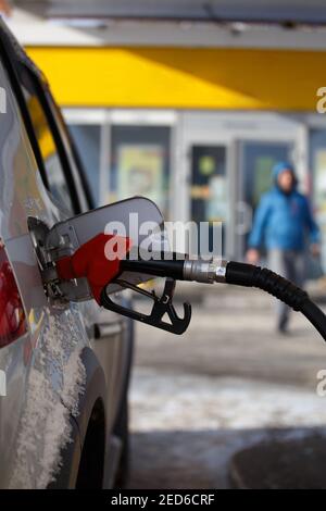 Silberne Metallic-Farbe Auto tanken an Wintertag Tankstelle - Nahaufnahme mit selektivem Fokus und verschwommen Mann Silhouette im Hintergrund. Stockfoto