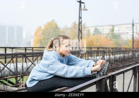 Junge aktive Sportlerin auf Brücke mit gestreckten Armen und stehen Rechtes Bein auf metallischem Zaun und Training am Morgen Im Freien Stockfoto