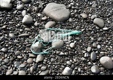 Fragmente von Plastikseil, die auf Kieselsteinen am Strand weggeworfen werden. Keine Personen. Stockfoto