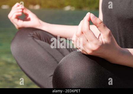 Frau, die Yoga praktiziert oder in der Nähe des Sees über die Natur meditiert. Nahaufnahme der Hände der Frau. Stockfoto