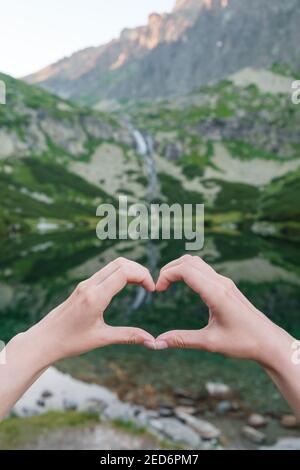 Frauen, die mit ihren Händen Herzform gegen die Berge nahe dem See Formen. Stockfoto