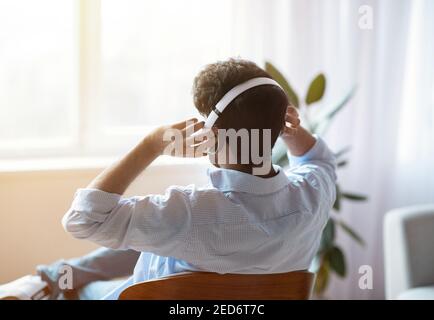 Unverkennbarer Mensch Hörmusik In Kabellosen Kopfhörern Zu Hause, Rückansicht Stockfoto