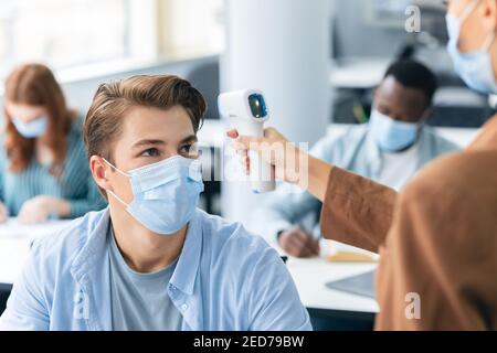 Lehrer mit berührungslosem Thermometer, das die Temperatur des Schülers misst Stockfoto