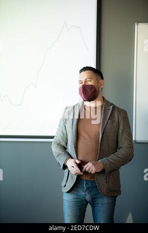 Junge Business Coach in Casualwear und Schutzmaske stehen zur Verfügung Whiteboard mit Grafik und Beantwortung von Fragen nach der Präsentation Stockfoto