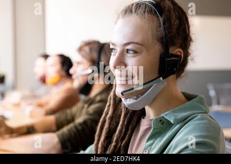 Reihe von Kundendienstmitarbeitern mit Headsets an Schreibtischen In einem modernen Callcenter mit junger weiblicher Bedienperson vor dem Hotel Stockfoto