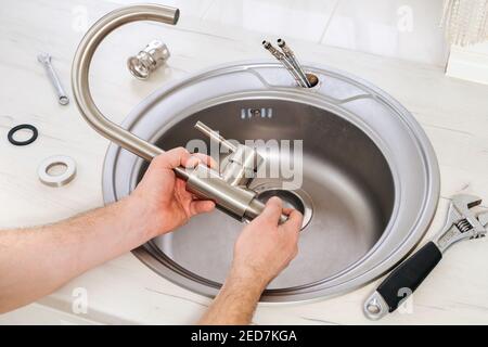 Klempner Hand hält einen neuen Wasserhahn für die Installation in der Spülbecken in der Küche Stockfoto