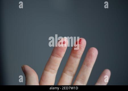 Finger auf der linken Hand ist geschnitten und blutet mit hellrotem Blut, selektiver Fokus, verschwommener dunkler Hintergrund Stockfoto