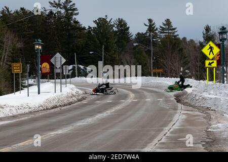 Zwei Schneemobile überqueren die Autobahn am Lake Pleasant in Speculator, NY an einem Winternachmittag. Stockfoto