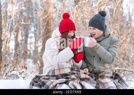 Liebesgeschichte. Das junge Paar im Winter Park ist in eine Decke gewickelt und trinkt Tee Stockfoto