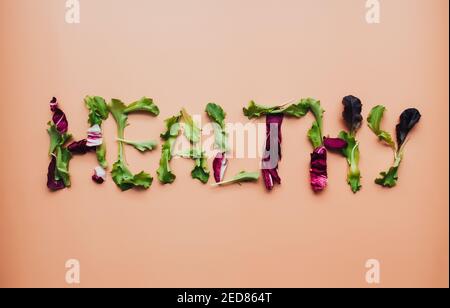 Text gesund mit grünen und violetten Salatblättern Mischung auf beigem Hintergrund. Hochwertige Fotos Stockfoto