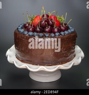 Hausgemachte Schokolade Geburtstagskuchen mit frischen Erdbeeren, Kirschen und Heidelbeeren auf einem weißen Kuchen stehen gekrönt Stockfoto