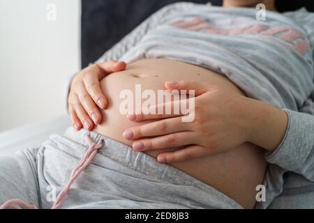 Seitenansicht auf dem Mittelteil der schwangeren kaukasischen Frau, die darauf liegt Das Bett mit dem Bett hält Bauch - Schwangerschaft Konzept Stockfoto