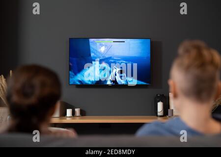 Rückansicht von zwei zeitgenössischen Geschwistern, die vor sitzen fernseher und Videospiel im Wohnzimmer während der Ferien Oder am Wochenende Stockfoto