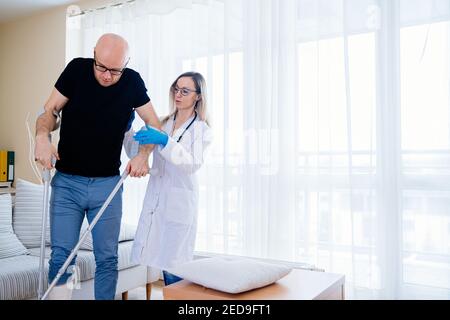 Eine junge Ärztin hilft dem behinderten Patienten auf Krücken zu gehen. Stockfoto