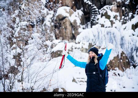 Erfolgreiche, lächelnde Klettererin mit Eispickel in der Hand auf einer verschneiten Landschaft. Stockfoto