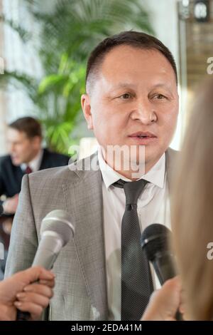 Reife asiatische männliche Delegierte in formalwear stehen vor Journalisten mit Mikrofonen und beantworten ihre Fragen im Interview Stockfoto