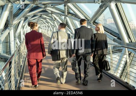 Rückansicht von mehreren ausländischen Delegierten in eleganten Anzügen diskutieren Bedingungen ihrer neuen Partnerschaft beim Umzug entlang Gang innen Business Center Stockfoto