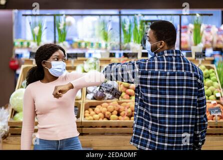 Millennial schwarze Frau und Mann in Gesichtsmasken Gruß jeder Andere durch Berühren Ellbogen im Supermarkt während covid-19 Stockfoto