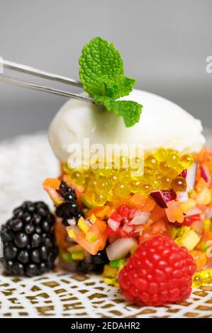 Close up view of fine cuisine chef placing mint leave on the top of served dish with kitchen tweezers while decorating it. High quality photo. Stockfoto