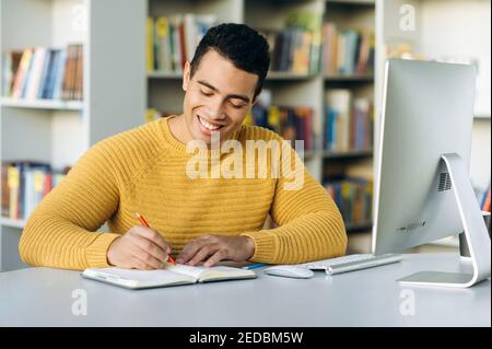 Online-Lernen. Attraktiver hispanischer junger Mann lernt online per Videoanruf, er notiert während des Unterrichts konzentriert Informationen, während er am Schreibtisch sitzt Stockfoto