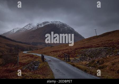 Brücke in der Nähe des Flusses Etive, Glencoe, Schottland, Großbritannien. Fluss mit viel Wasser, Bild im Wald mit dem Stob Dearg Berg im Hintergrund. Verschneite atmo Stockfoto