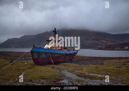 Verlassene Fischerboot gestrandet an Land in den schottischen Highlands, Großbritannien. Verlassen, rostig und baufällig. Stürmischer Tag mit vielen Wolken und Nebel in der Env Stockfoto