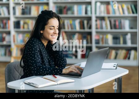 Schöne junge Erwachsene Frau sitzen am Schreibtisch im modernen Büro, mit Computer. Wunderschöne stilvolle weibliche Mitarbeiter arbeiten an Projekt oder Mädchen Student schriftlich Notizen auf Online-Vorlesung Stockfoto