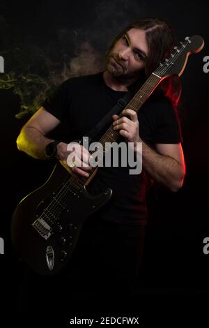 Junger Mann mit sehr langen Haaren, der seine Gitarre hält Singen Stockfoto