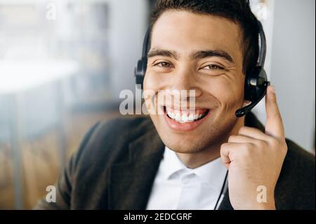 Porträt des hispanischen Betreibers des Callcenters. Zufriedener männlicher Berater, der am Schreibtisch sitzt, das Headset trägt, blickt mit freundlichem Lächeln direkt auf die Kamera Stockfoto
