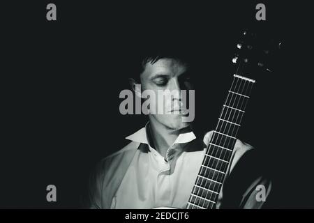 Junger Mann, der auf den Hals einer klassischen Gitarre schaut. Schwarz-Weiß dramatisches Porträt, Low-Key. Stockfoto