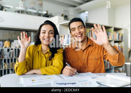 Glückliche multirassische Kollegen auf Videokonferenz. Fröhliche Geschäftspartner kommunizieren mit anderen Kollegen, diskutieren über das Projekt, winken die Hände, grüßen Stockfoto