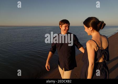 Porträt eines jungen glücklichen Paares in der Liebe auf dem Hintergrund des Meeres in der Sonnenuntergang Beleuchtung. Stockfoto