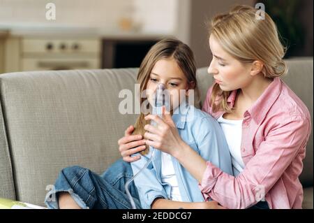 Eine fürsorgliche traurige Mutter macht Inhalationen mit Inhalator zu ihrer geliebten kleinen kranken verärgerten Tochter. Das Kind erkrankte an Grippe, Husten, laufender Nase Stockfoto