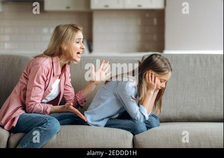 Böse Mutter schimpft kleine Tochter im Wohnzimmer, Eltern lehrt ein frech schelmisch Kind, Kind Mädchen empört sich über Strafe und Entzug der Unterhaltung Stockfoto