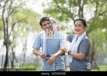 Asiatische Paare mittleren Alters trainieren zusammen mit einem Roller im Stadtpark, Frau wischte den Schweiß aus ihrem Mann nach dem Training. Stockfoto