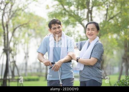 Asiatische Paare mittleren Alters trainieren zusammen mit einem Roller im Stadtpark, Frau wischte den Schweiß aus ihrem Mann nach dem Training. Stockfoto