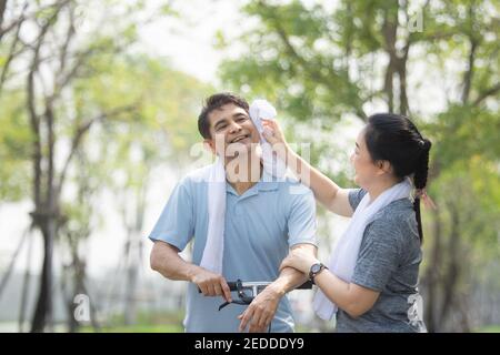 Asiatische Paare mittleren Alters trainieren zusammen mit einem Roller im Stadtpark, Frau wischte den Schweiß aus ihrem Mann nach dem Training. Stockfoto