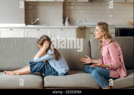 Seitenansicht der schreienden Mutter, schreit kleine Tochter an, die sie schimpft. Das kleine Mädchen ignoriert Mama, schließt ihre Ohren mit den Armen. Komplizierte Beziehungen von Mutter und Kind Stockfoto