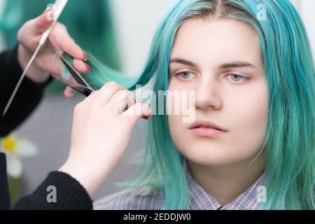 Hairstylistin Hände schneiden Haar der Schönheit Frau mit langen grünen Haaren mit Schere. Haarpflege im professionellen Schönheitssalon Stockfoto