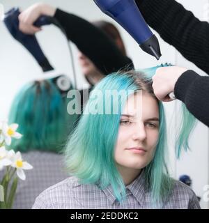 Portrait der schönen jungen Frau mit langen grünen Haaren beim Trocknen und Styling Haar im Schönheitssalon. Brunette Friseur trocknet Kundenhaar Stockfoto