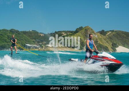 Ein Mann auf einem Tragflächenboot Surfbrett wird von einem Mann auf einem Jetski in einem türkisfarbenen Meer, klaren blauen Himmel, Sommertag geschleppt. Stockfoto