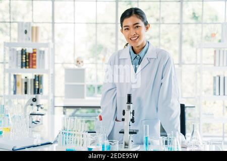 Portrait von erfolgreichen und schönen jungen asiatischen medizinischen Forscherin Und Wissenschaftler tragen Labcoat stehen im Labor während der Arbeit an Entwicklung eines Covid-19-Impfstoffs Stockfoto