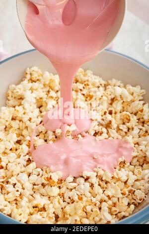 Gießen von geschmolzenem Marshmallow in Schüssel mit Popcorn auf Licht Hintergrund Stockfoto