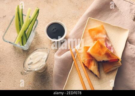 Teller mit leckeren frittierten Frühlingsrollen und Soßen auf Licht Hintergrund Stockfoto