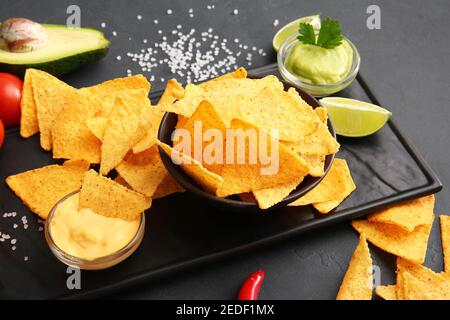 Leckere Nachos und Saucen auf dunklem Hintergrund Stockfoto