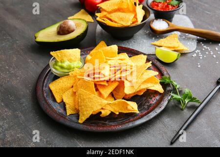 Teller mit leckeren Nachos und Produkten auf dunklem Hintergrund Stockfoto