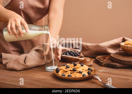 Frau mit leckeren Pfannkuchen, frische Heidelbeere und Milch auf farbigem Hintergrund Stockfoto